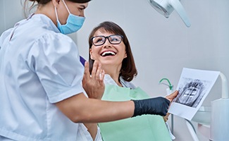 Woman smiling with dentist while reviewing X-ray