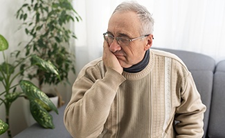 Senior man on couch with pain in mouth